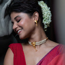 Elegant model wearing a gold-plated choker and earrings with white beads, styled with a red saree and floral hair accessory.
