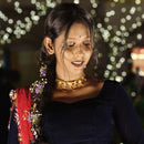 Model wearing a gold-plated choker necklace and traditional attire with twinkling lights in the background.